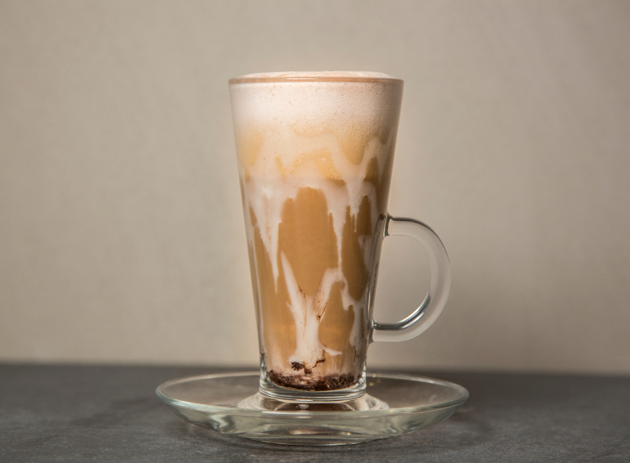 White Chocolate Mocha dripping over the edge of a clear glass mug on to a clear small saucer